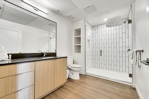 A modern bathroom with a wooden vanity, a white toilet, and a walk-in shower with a tiled wall.