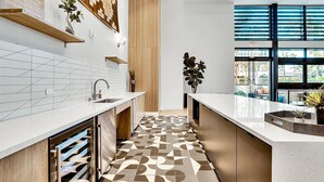 A modern kitchen with a geometric patterned floor, wooden shelves, and a view through large windows.