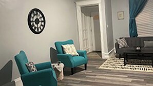 A living room with teal armchairs, a dark sofa, and a patterned rug.