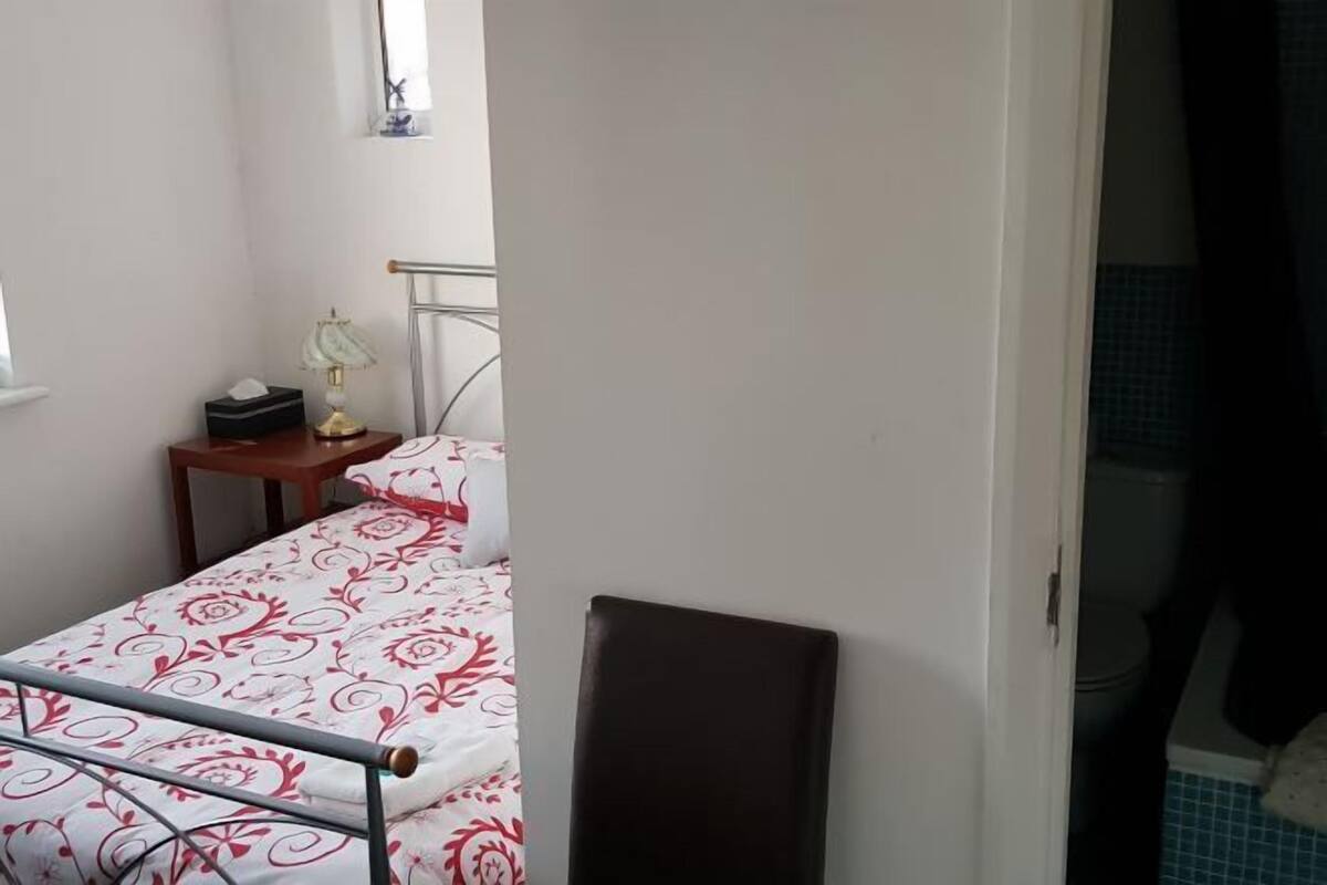 A bedroom with a bed, a bedside table with a lamp, and a window.