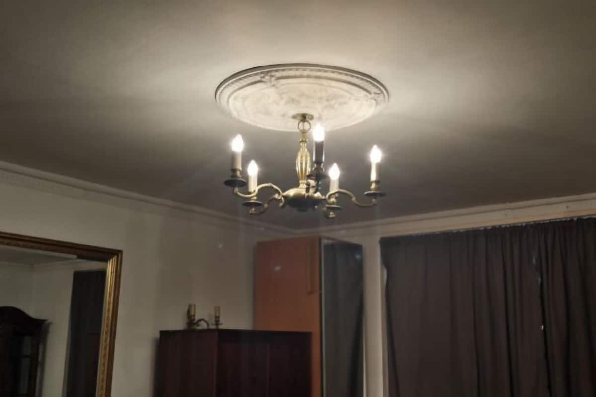 A room with a chandelier, a mirror, a wooden cabinet, and a curtain.
