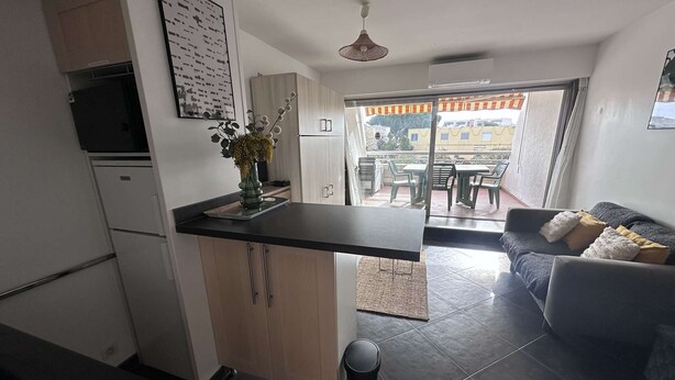 A modern kitchen with a central island, a dining area with a table and chairs, and a sofa with cushions. - Air-conditioned Studio-Cabin for 4 pers. with private parking, near beach in Port Camargue (Le Grau-du-Roi)