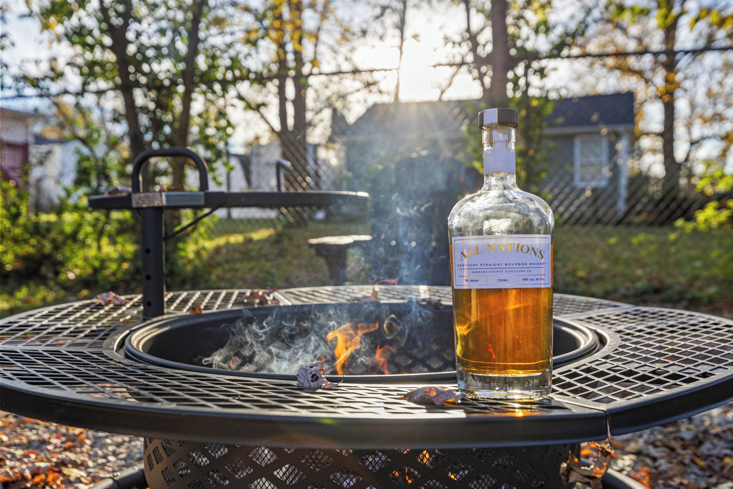 A bottle of Kentucky Straight Bourbon Whiskey on a metal table outdoors with a fire pit in the background.
