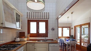 Una cocina con estufa, pileta y lavavajillas, muebles de madera y un ventanal con cortinas.