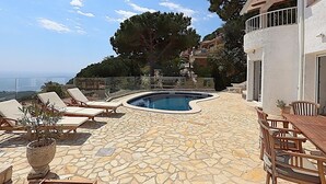 Un área de piscina con piso de piedra, sillas de descanso y una mesa de comedor.