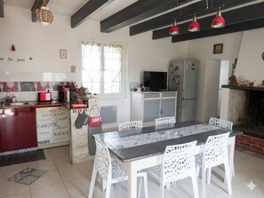 A kitchen with a dining table, chairs, a refrigerator, and a television.