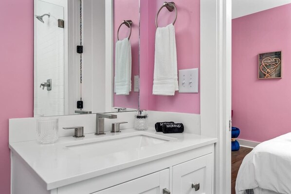 Un baño moderno con un tocador blanco, un espejo grande y una pared rosa.