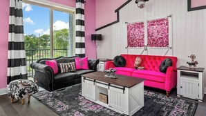 A living room with a black and white striped curtain, a black leather sofa with pink and black cushions, a red sofa with black cushions, a wooden coffee table, and a white cabinet.