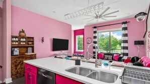 A kitchen with pink cabinets, a white countertop, and a stainless steel sink.