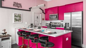A modern kitchen with pink cabinets, a stainless steel refrigerator, and a bar area with black chairs.