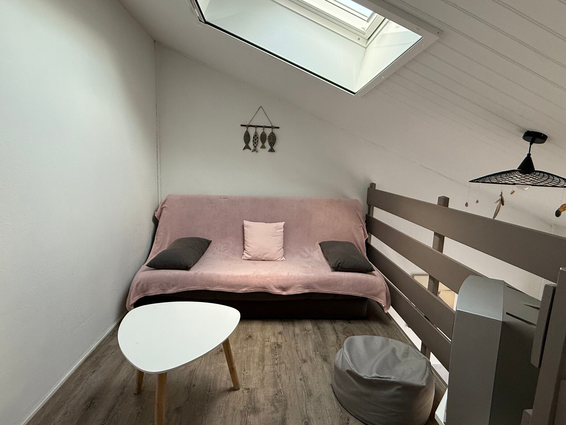 A small, cozy room with a pink sofa, a white table, and a skylight above.