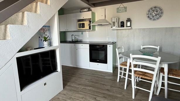 A compact kitchen with white cabinets, a microwave, and a stove. There is a dining area with a round table and white chairs.