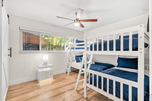 Une chambre d’enfant avec des lits superposés, un bureau, une chaise et un ventilateur de plafond.