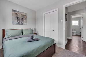 Ein Schlafzimmer mit einem Bett, Kissen, einem Gemälde und einer Tür zu einem Badezimmer.