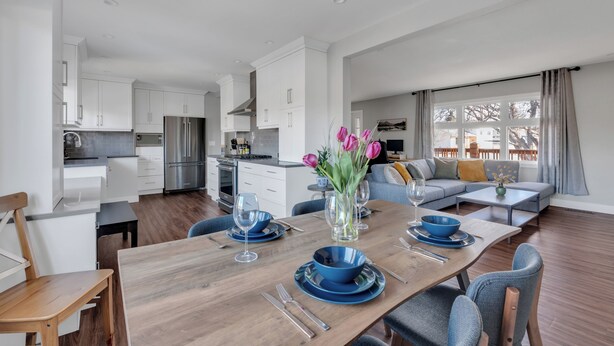 A modern kitchen with white cabinets, a stainless steel refrigerator, and a dining area with a wooden table set for four.