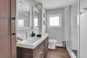 Ein modernes Badezimmer mit großem Spiegel, Waschbecken in Weiß, Toilette und einer Duschkabine aus Glas.