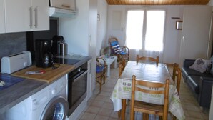 Cocina compacta con lavadora, cafetera y comedor con mesa y sillas.