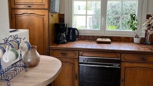 Een keuken met houten kastjes, een koffiezetapparaat, een vaatwasser en een raam met uitzicht op groen.