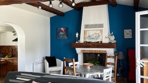 Een kamer met een bed, een eettafel met stoelen, een open haard en een keukenhoek.