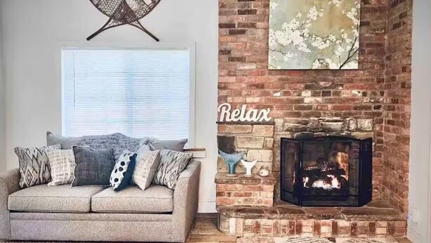 Un salon chaleureux avec une cheminée, un canapé agrémenté de coussins à motifs et une fenêtre avec des stores.