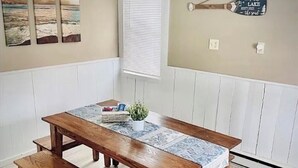 Une table de salle à manger en bois, accompagnée de bancs, d’une plante en pot et d’un panneau décoratif accroché au mur.