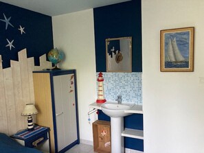 Ein Schlafzimmer mit Bett, Nachttisch, Kommode, Globus, Spiegel, Waschbecken und einem Gemälde.