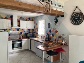 Eine Küche mit weißen Schränken, einer Mikrowelle, einem Toaster und einer Kaffeemaschine. Eine farbenfrohe, diamantmusterige Spritzschutzleiste und eine Uhr sind an der Wand angebracht.