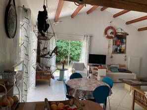Ein Zimmer mit Esstisch, Stühlen, einer Couch, einem Fernseher und einer Pendelleuchte.