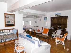 Un salon comprenant un canapé, des fauteuils, une table et un coin cuisine avec des placards.