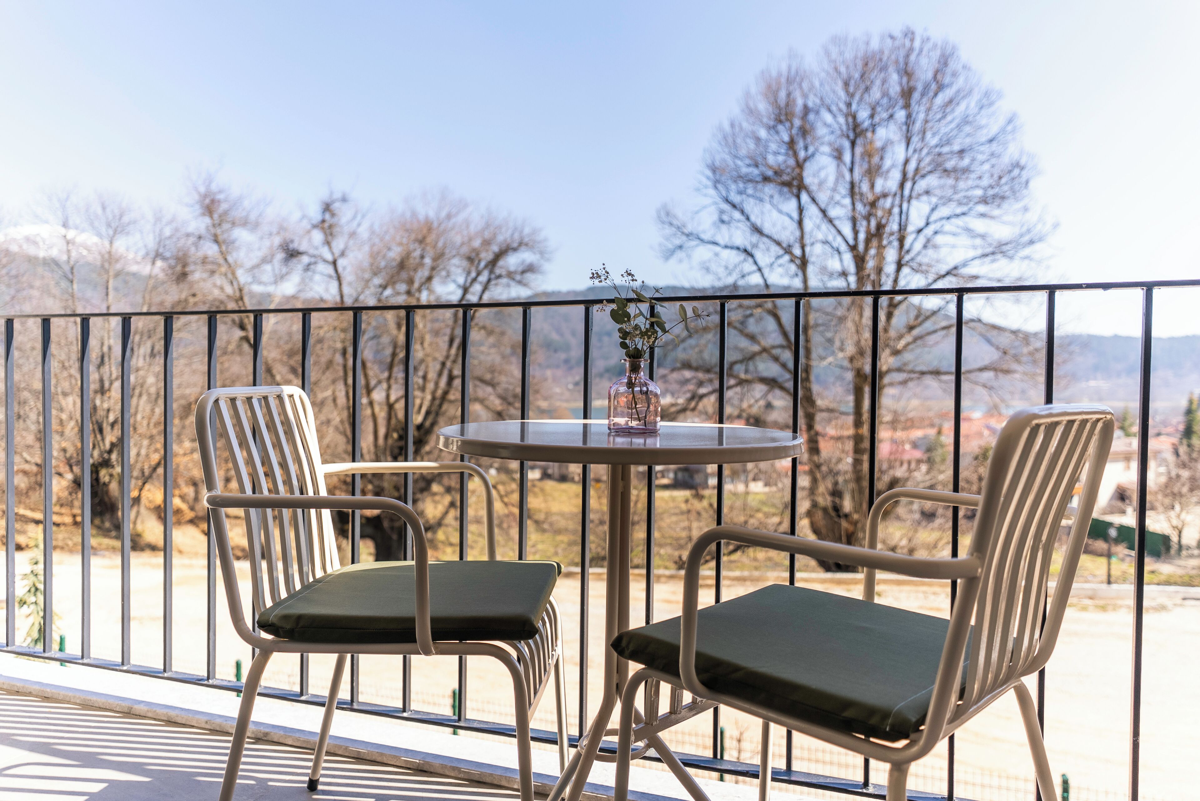 A balcony with two chairs and a table, a vase with flowers, and a view of trees and mountains.