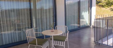 Un balcón con mesa y sillas, puertas correderas de vidrio grandes y vistas al exterior.