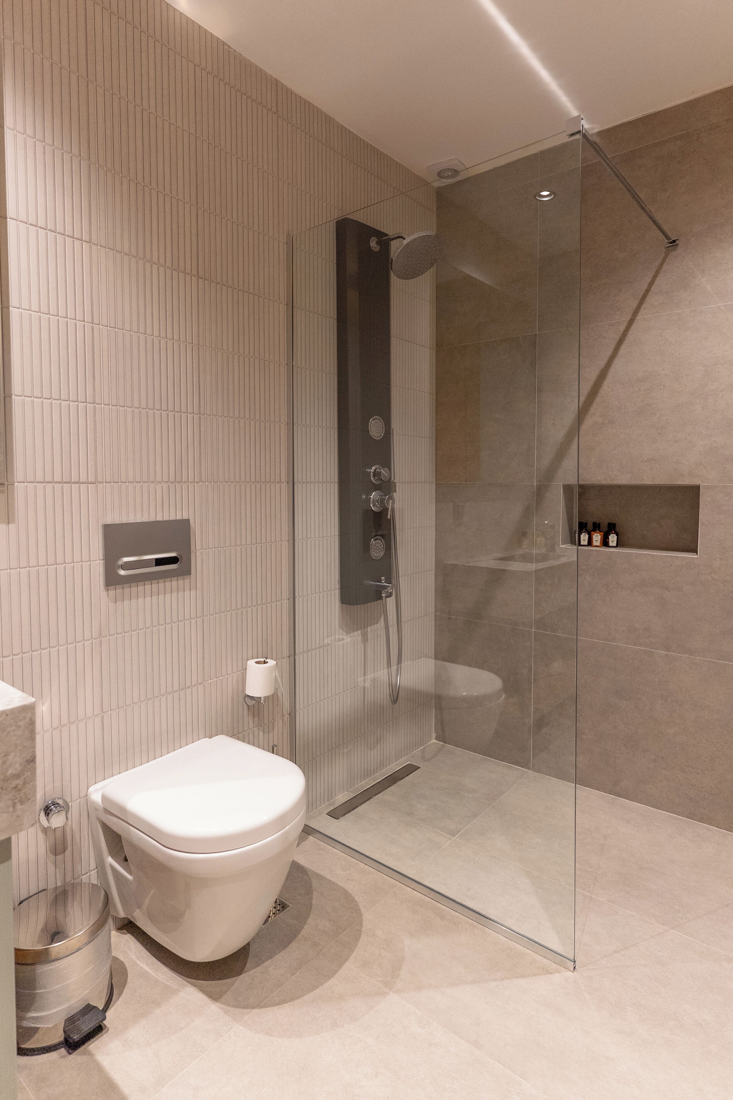 A modern bathroom with a glass-enclosed shower, a toilet, and a small shelf with toiletries.