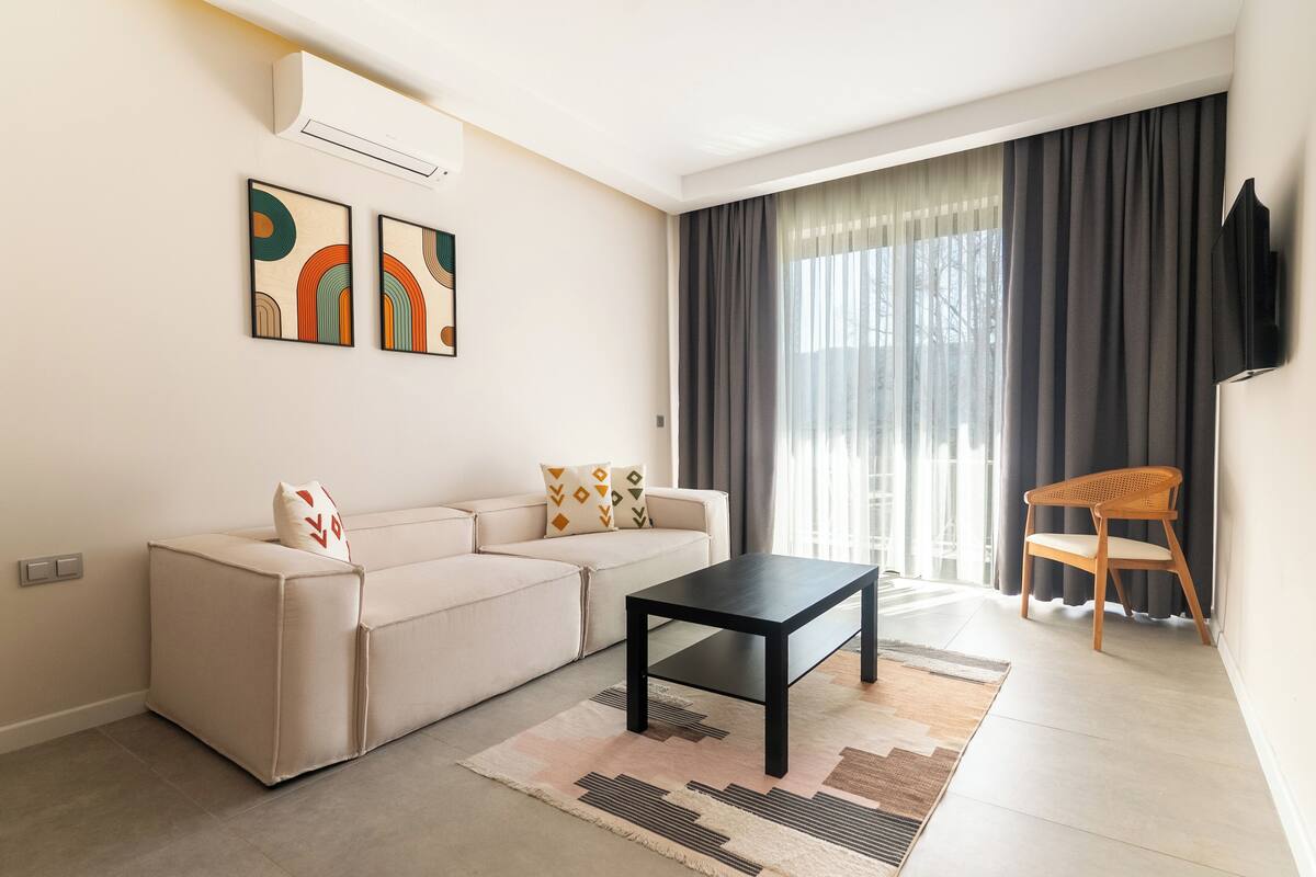 Uma sala de estar moderna com um sofá, uma mesa de centro e uma poltrona. Há uma TV de tela plana fixada na parede.