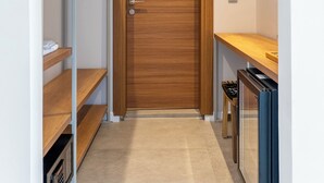 A narrow hallway with a wooden door, a metal shelf unit with folded clothes, and a small table with a chair. - Bade Gölcük (Odemis)