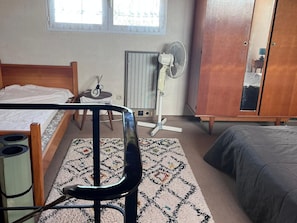 A bedroom with a bed, a desk, a chair, a wardrobe, a radiator, and a window.