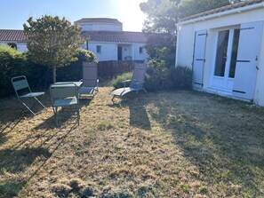 A backyard with a white building, a covered patio area, and a lawn with chairs.