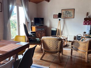 A living room with a dining table, chairs, a television, a floor lamp, and a sofa.