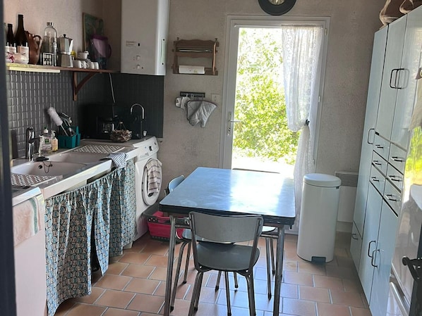A compact kitchen with a washing machine, a sink, a table with chairs, and a cabinet with drawers.