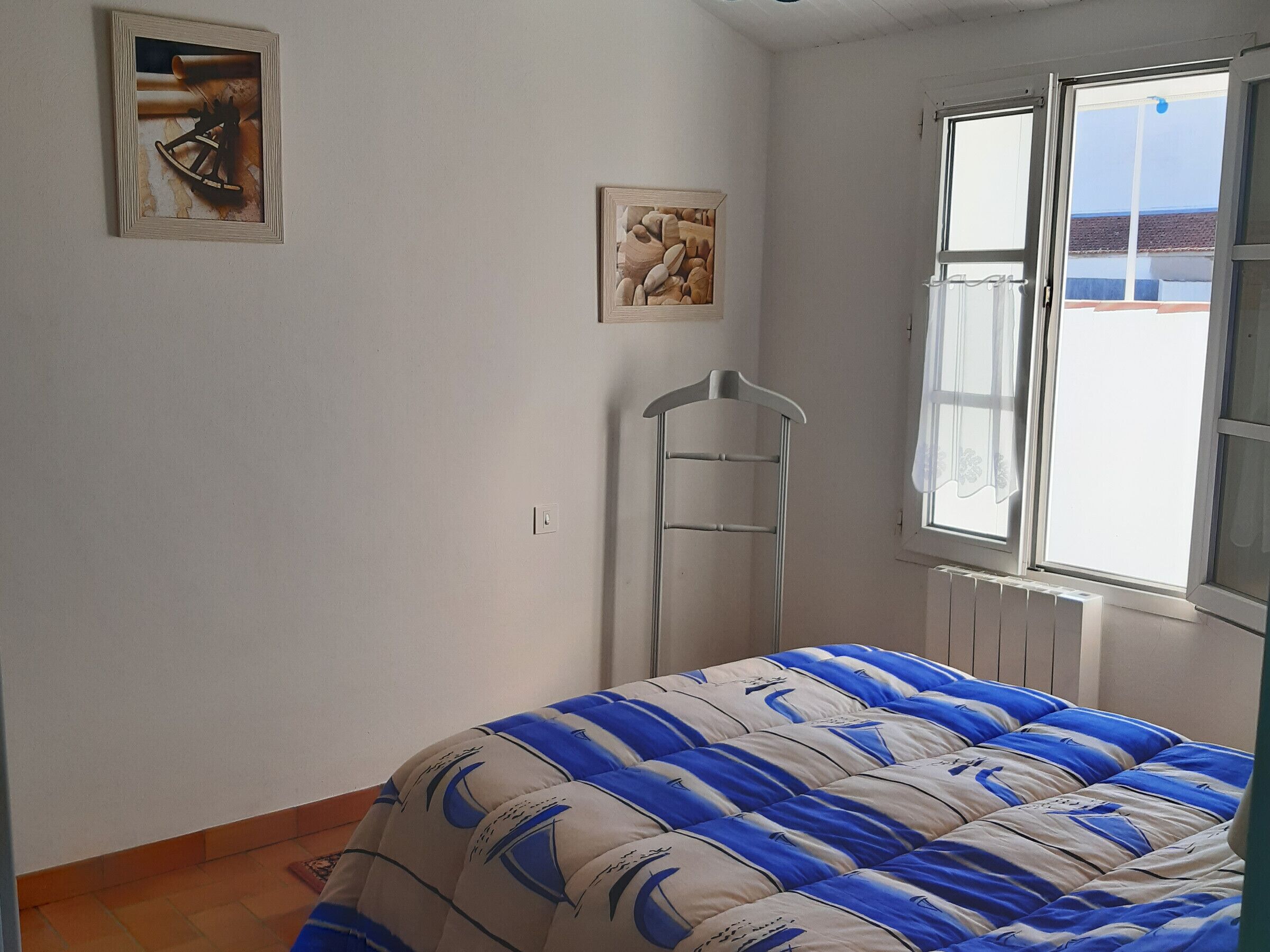 Une chambre à coucher avec un lit, une fenêtre, un radiateur et deux tableaux accrochés au mur.