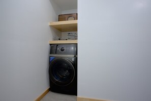 Compact laundry room with a front-loading washing machine and storage for folded towels.