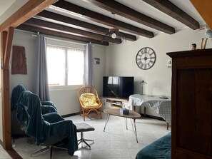 Uma sala de estar com sofá, poltrona, televisão, mesa e relógio na parede.