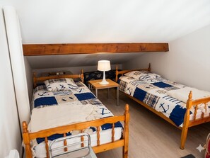 A small, cozy room with two wooden beds, a nightstand, and a lamp.