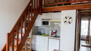 A kitchen with white cabinets, a microwave, and a coffee maker. There is a wooden staircase leading to a loft area.