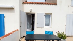 An outdoor patio area with a table and chairs, a small window, and a door leading to a room.