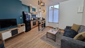 A modern living room with a flat-screen TV, a kitchen with a microwave, and a dining area with a table and chairs. - Modern and quiet studio downtown with secure parking (Châteauroux)