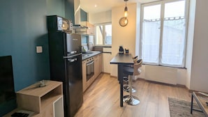 A modern kitchen with a black refrigerator, wooden cabinets, a stainless steel sink, and a dining area with a bar stool. - Modern and quiet studio downtown with secure parking (Châteauroux)