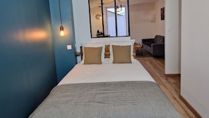 A modern bedroom with a large bed, a blue accent wall, and a view into an adjacent living area. - Modern and quiet studio downtown with secure parking (Châteauroux)