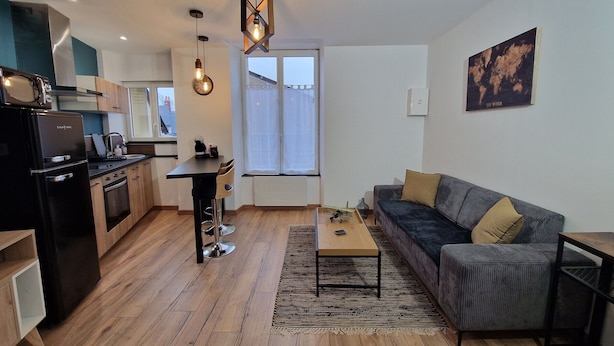 A modern apartment with a kitchen, dining area, and living room. It features a large window, a sofa, and a coffee table. - Modern and quiet studio downtown with secure parking (Châteauroux)