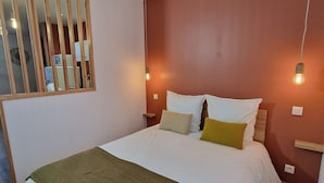 Una cama bien hecha con ropa blanca y una manta verde, cabecera de madera y lámparas de noche.