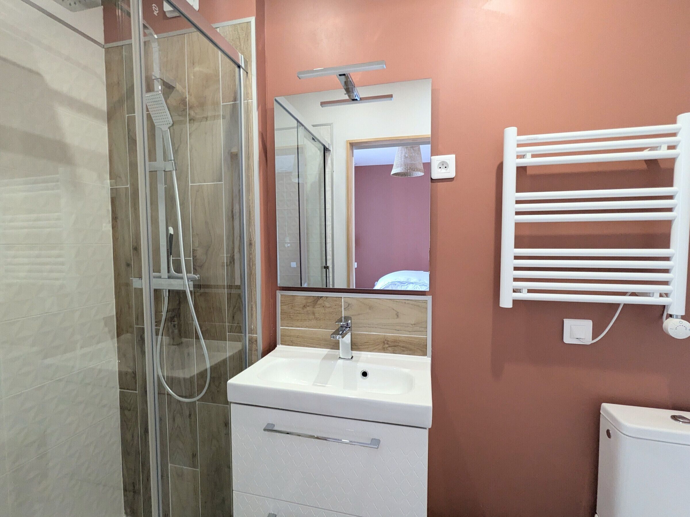 Een moderne badkamer met een douchecabine van glas, een witte wastafel en een spiegel erboven.